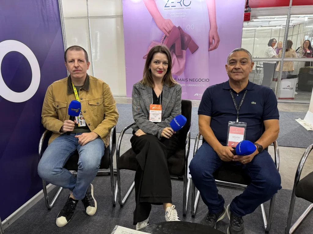 Dois homens e uma mulher sentados em cadeiras com microfones nas mãos