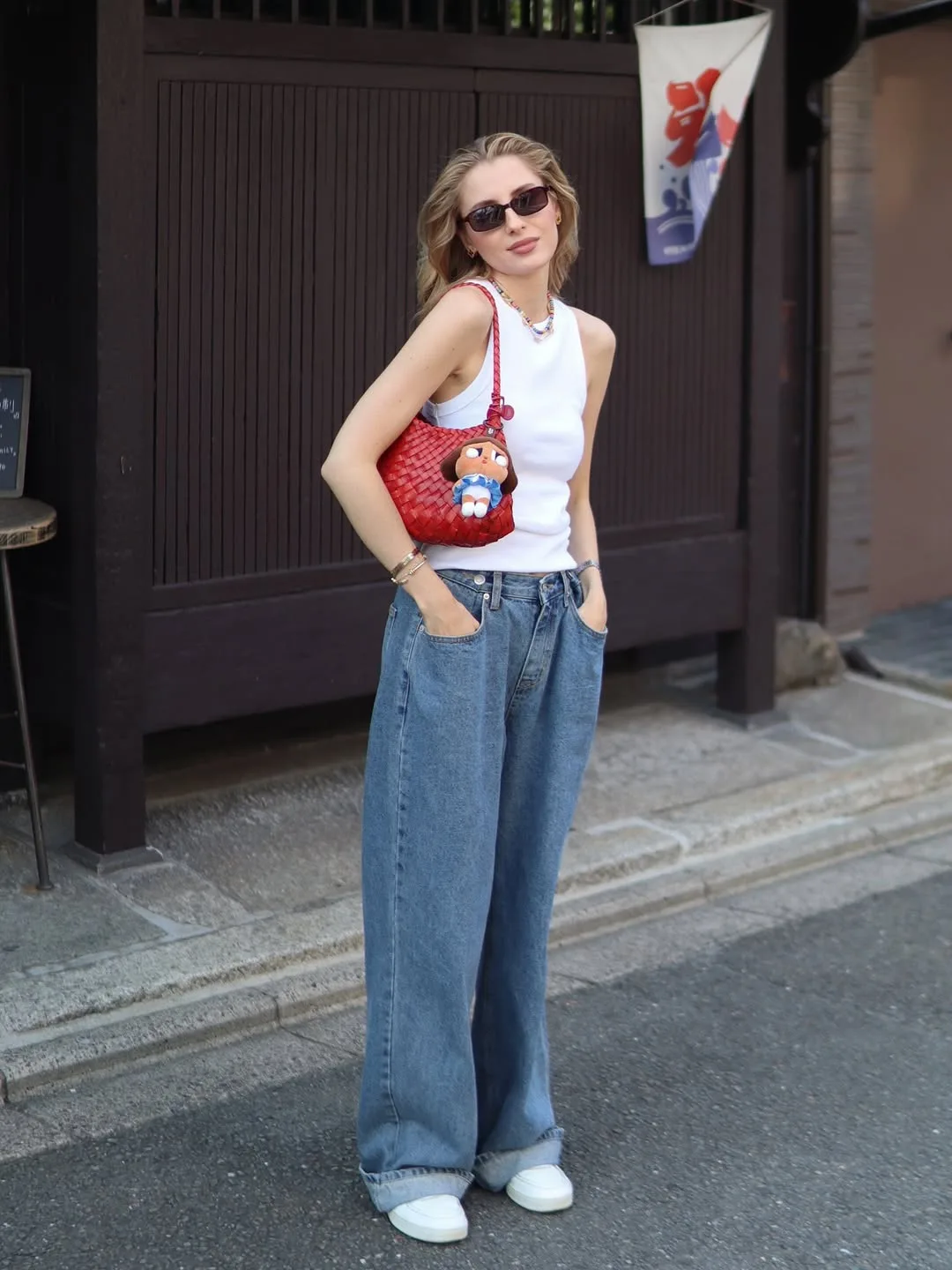 Mulher jovem com blusa branca, calça jeans, bolsa vermelha, óculos de sol e tênis branco