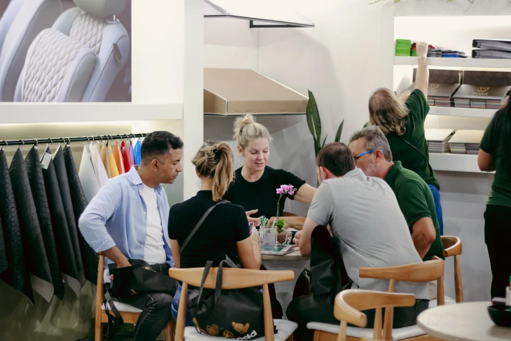 Pessoas sentadas ao redor de uma mesa e arara com couros atrás